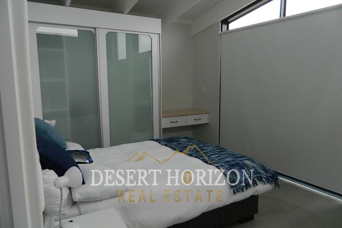 A modern bedroom featuring a built-in wardrobe with frosted glass doors, a floating vanity desk, and a raked ceiling with a high-level window.