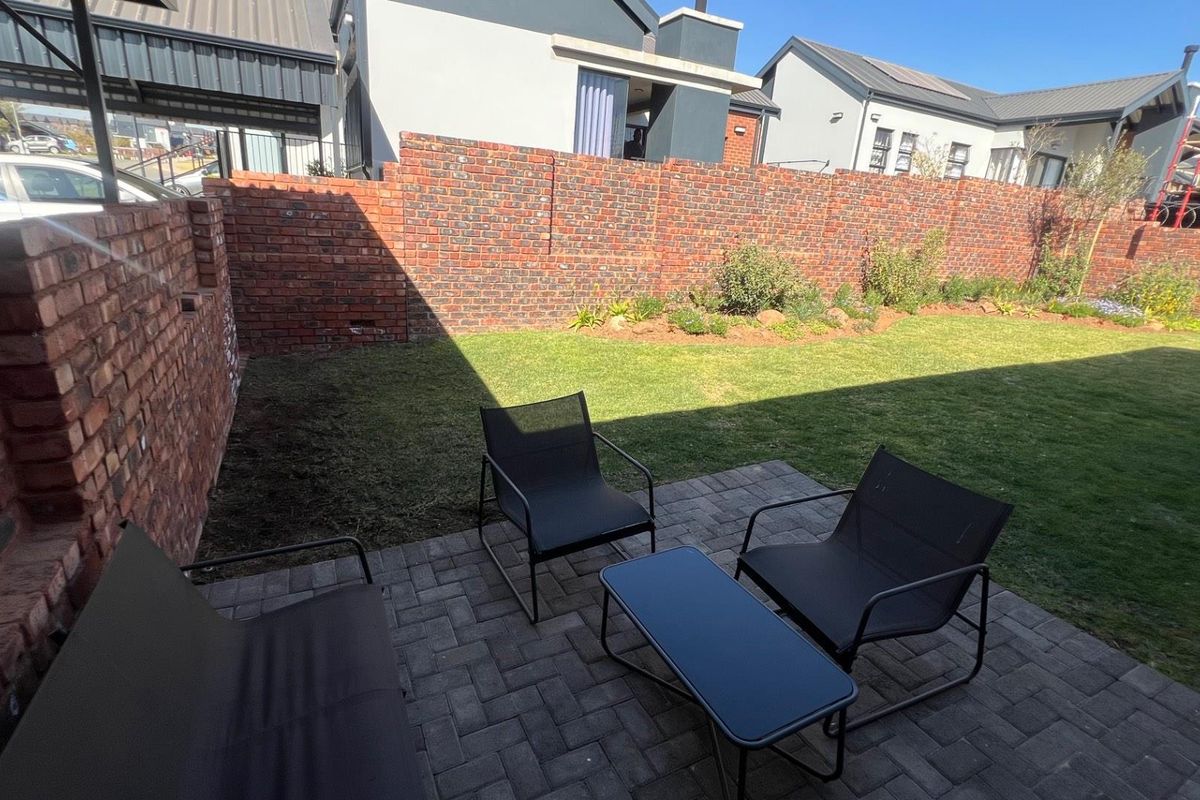 A private rear garden featuring a paved patio area and a well-maintained lawn enclosed by a brick boundary wall.