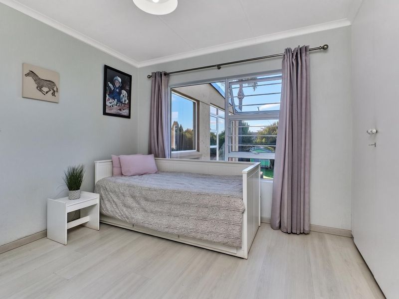 A bright bedroom featuring light-toned laminate flooring, a built-in cupboard, and a louvered window with curtain rod.