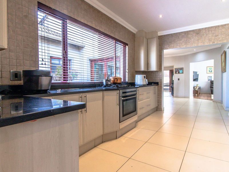 A functional kitchen featuring granite countertops, built-in oven, gas hob, tiled backsplash, and ample cabinetry, leading into an adjacent living area.