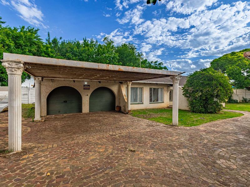 Front exterior view featuring a double garage, a large carport with decorative columns, and a paved driveway set within a landscaped garden.