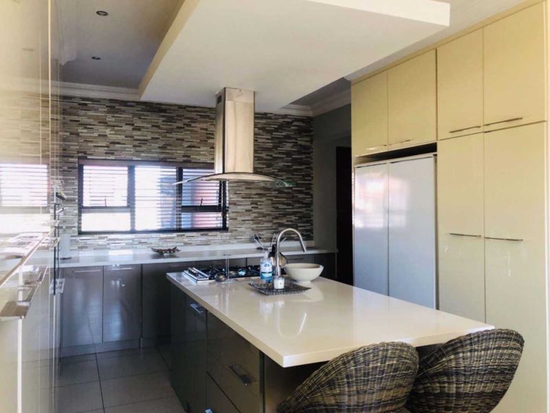 Modern kitchen featuring a central island with stone countertops, built-in cabinetry, a gas hob with extractor fan, and a decorative mosaic tile backsplash.