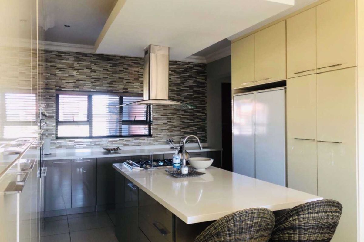 Modern kitchen featuring a central island with stone countertops, built-in cabinetry, a gas hob with extractor fan, and a decorative mosaic tile backsplash.