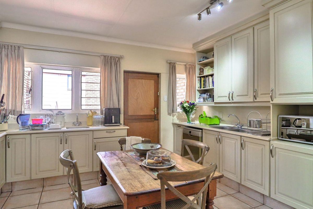 A functional kitchen featuring light-toned cabinetry, tiled flooring, dual stainless steel sinks, and ample counter space, providing a practical layout for daily meal preparation.
