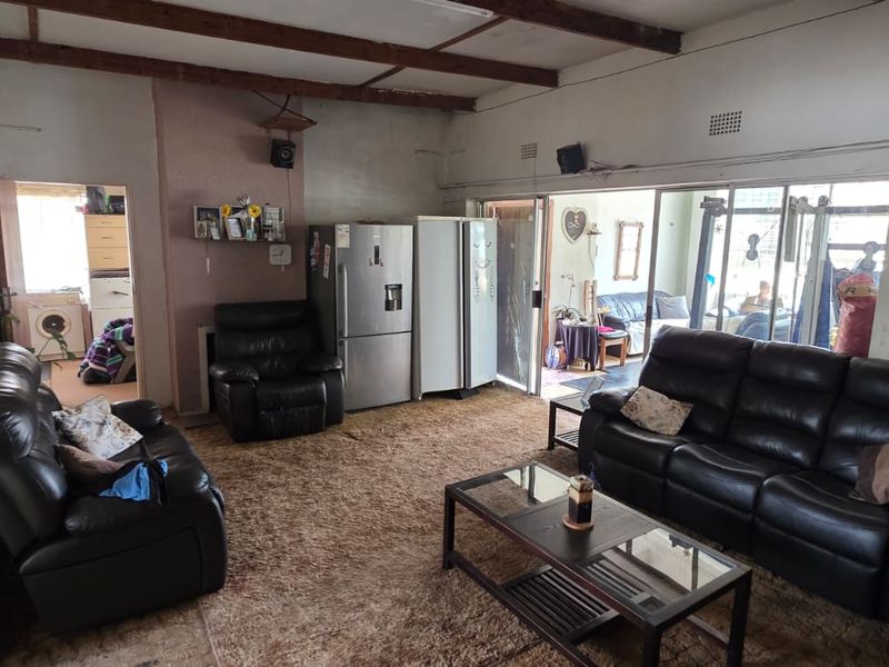 Spacious living area featuring exposed timber ceiling beams and large sliding glass doors leading to an adjacent room, requiring cosmetic updates to finishes.