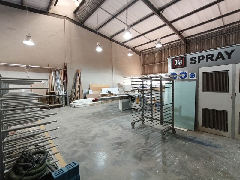 Industrial workshop space featuring a dedicated spray booth, high ceilings with exposed steel trusses, and durable concrete flooring suitable for manufacturing or fabrication.