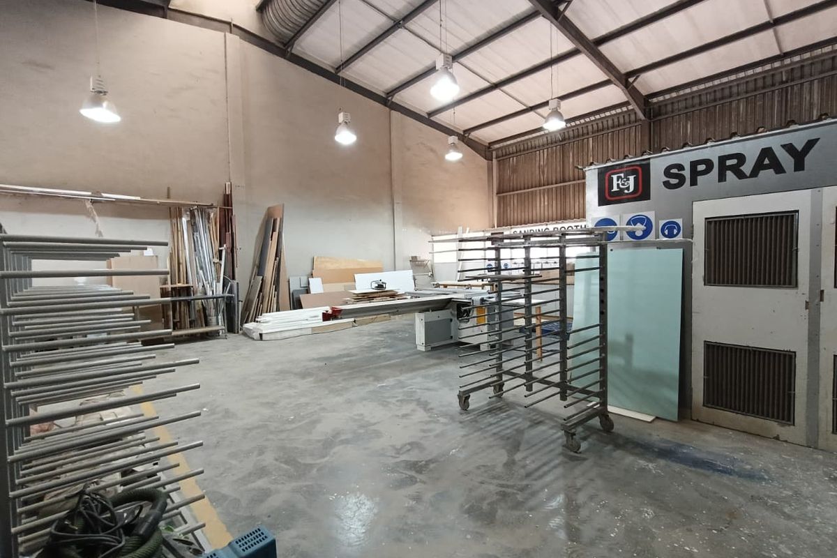 Industrial workshop space featuring a dedicated spray booth, high ceilings with exposed steel trusses, and durable concrete flooring suitable for manufacturing or fabrication.