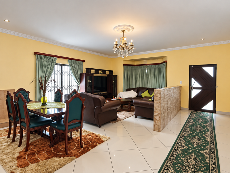 Open-plan living and dining area featuring tiled floors, a decorative stone-clad partition wall, crown molding, and a classic chandelier.