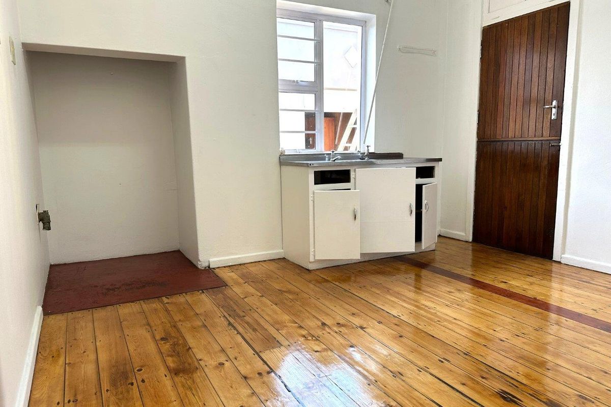 A basic utility or kitchen area featuring original timber flooring, a single sink unit, and a recessed alcove, offering potential for renovation.