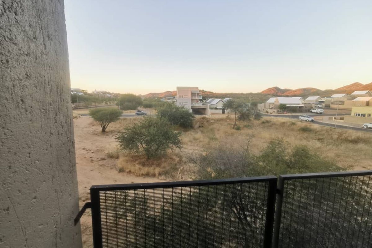 An elevated view from a balcony overlooking a dry landscape with surrounding residential properties and distant hills.