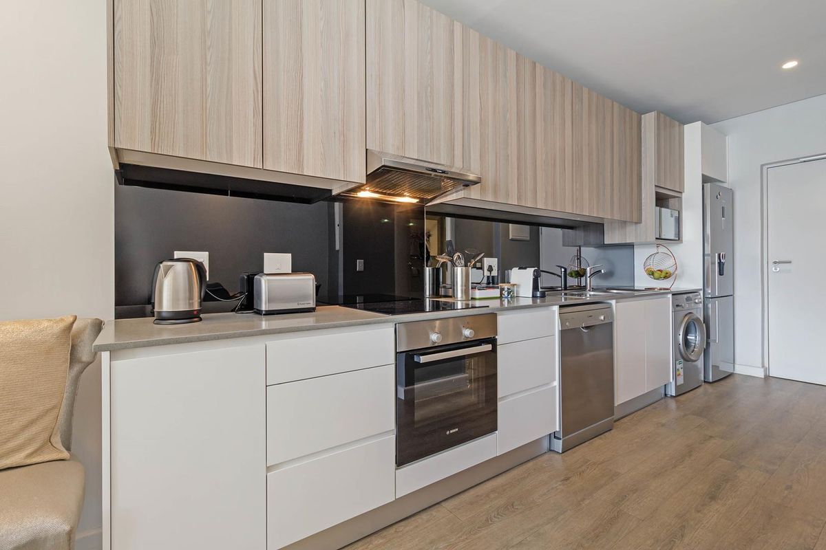 Modern kitchen featuring light wood-grain upper cabinetry, white lower cabinets, integrated appliances, and a sleek black splashback with high-quality finishes.