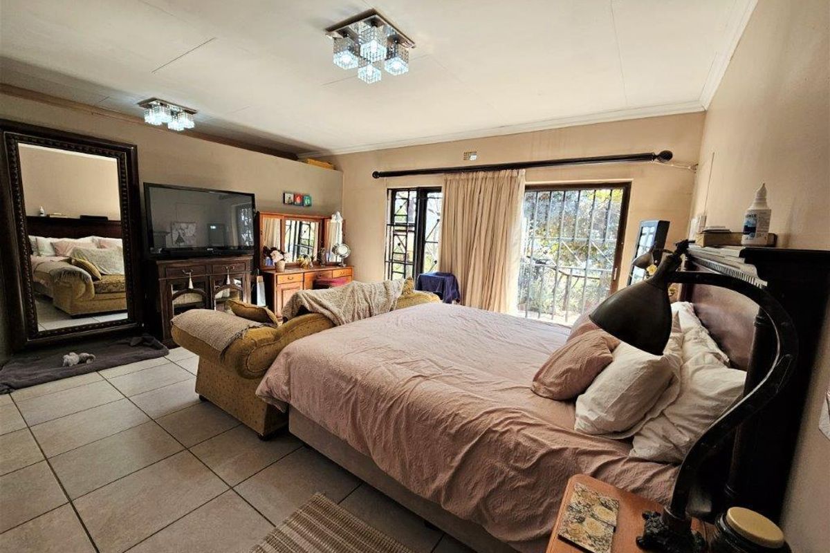 Spacious bedroom featuring tiled flooring, dual ceiling light fixtures, and sliding glass doors with security bars leading to an outdoor area.