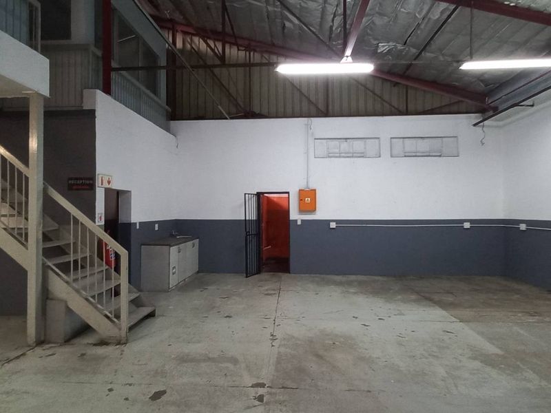 Spacious industrial utility area featuring a mezzanine level, metal staircase, exposed roof trusses, and durable concrete flooring, suitable for various commercial or storage uses.