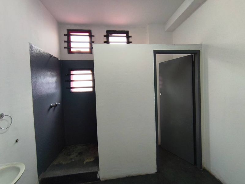 A functional industrial-style bathroom featuring a walk-in shower area with security bars on the windows and a separate doorway.