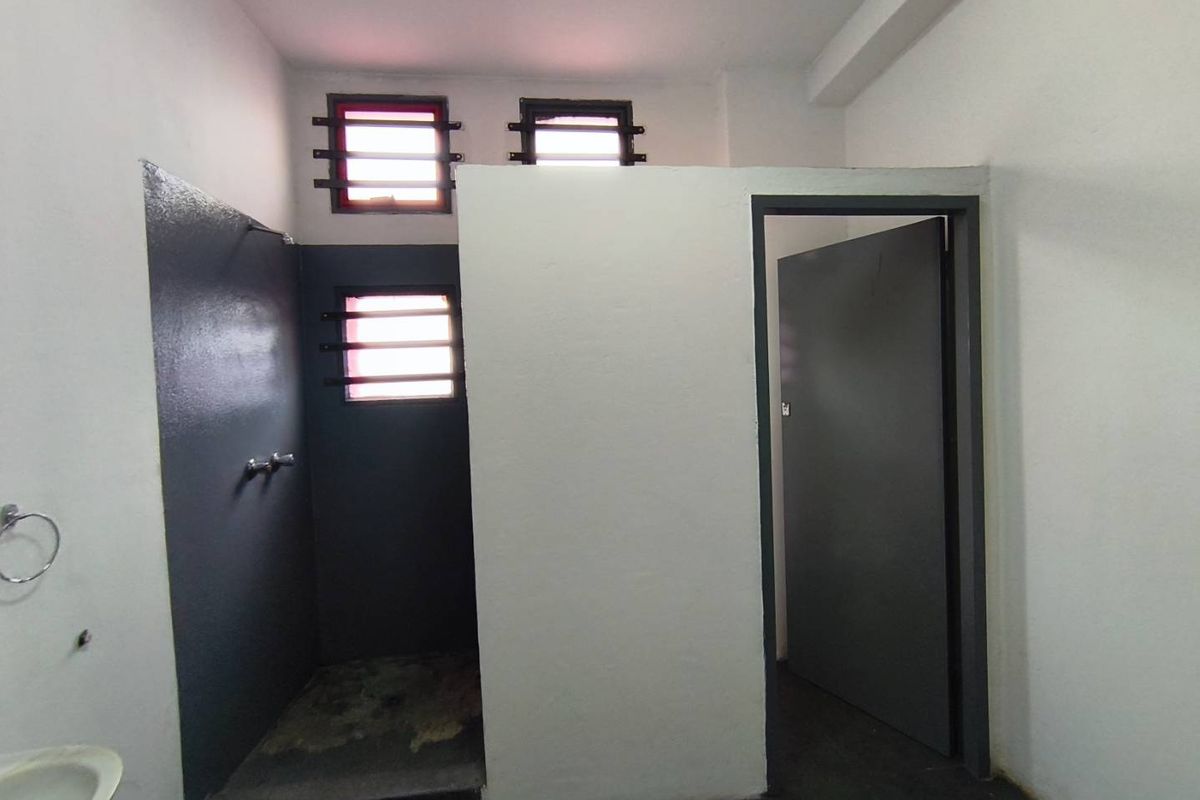 A functional industrial-style bathroom featuring a walk-in shower area with security bars on the windows and a separate doorway.