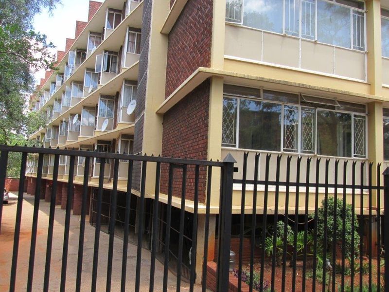 Exterior view of a multi-story apartment building featuring brick facade, metal security fencing, and multiple window units.