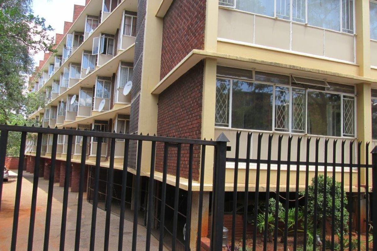 Exterior view of a multi-story apartment building featuring brick facade, metal security fencing, and multiple window units.