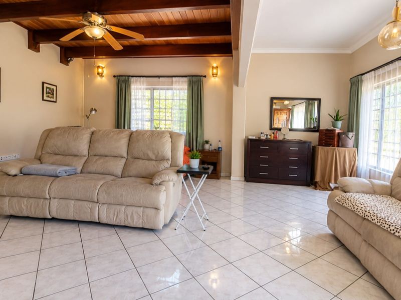 Spacious living room featuring exposed timber ceiling beams, tiled flooring, and large windows that provide ample natural light.