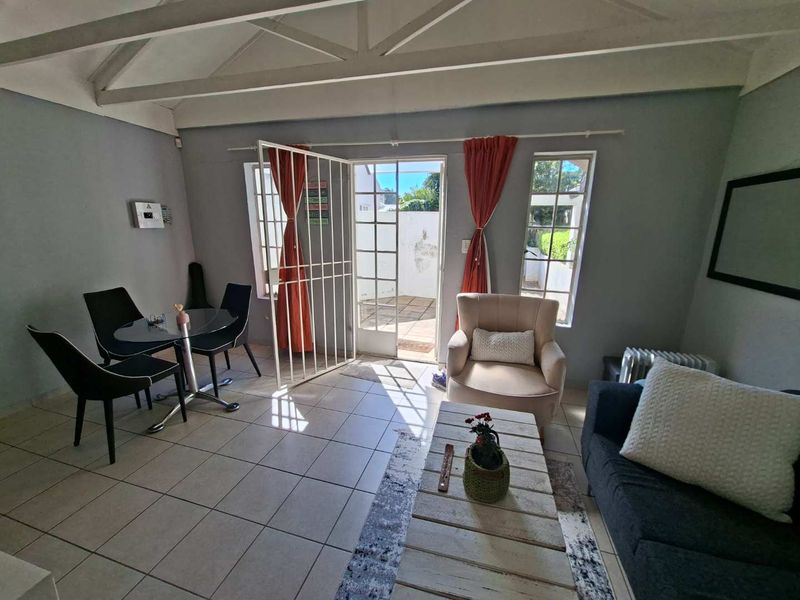 A bright living room featuring tiled floors, exposed roof trusses, and direct access to an outdoor patio through a security gate and french doors.