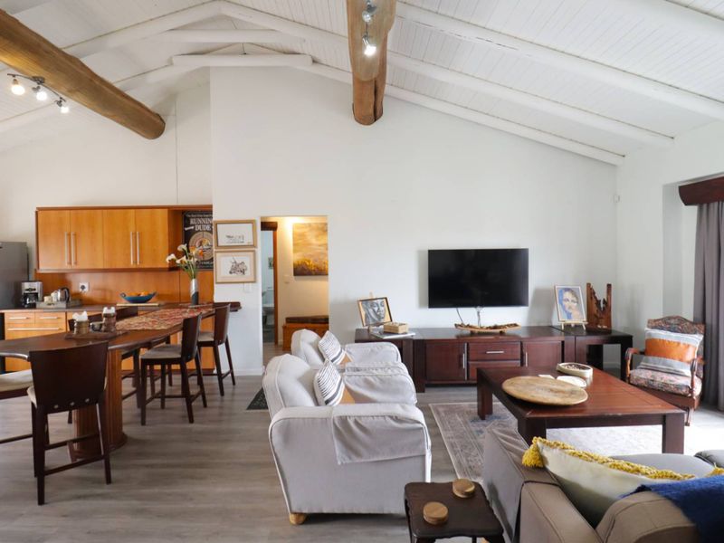 Spacious open-plan living area featuring a vaulted ceiling with exposed timber beams, integrated kitchen with breakfast bar, and modern laminate flooring.