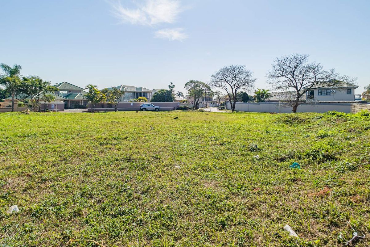 A vacant residential plot of land featuring open grassed space and perimeter boundary walls in a developed suburban neighborhood.