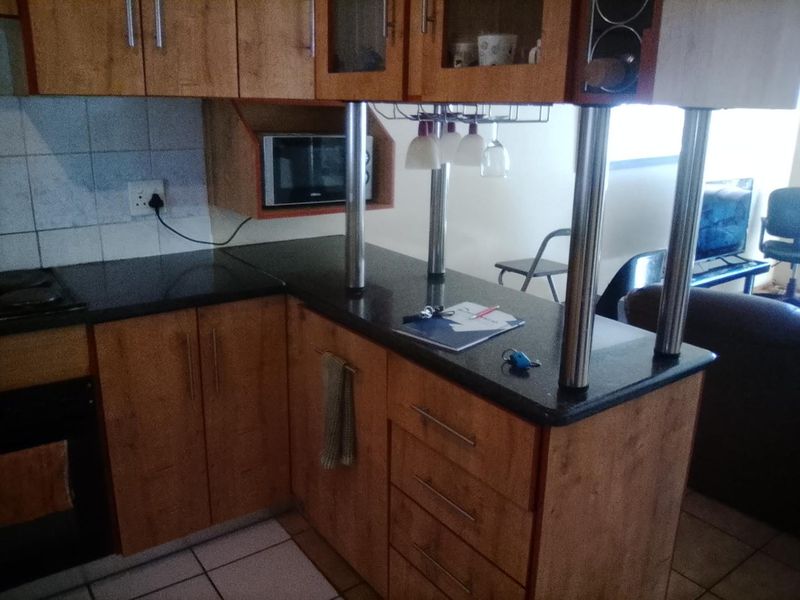 A functional kitchen featuring wood-look laminate cabinetry, dark granite countertops, a breakfast bar, and built-in appliances including an oven and microwave.
