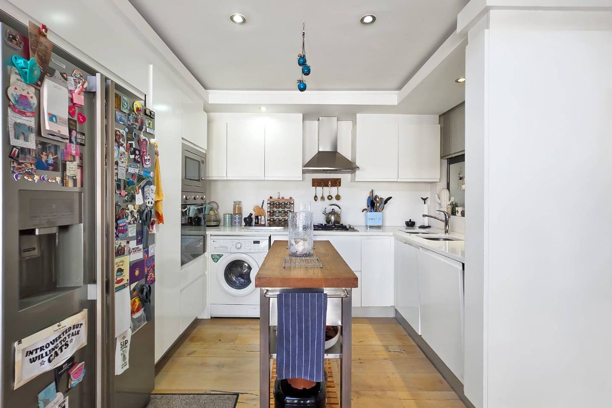 A modern, compact kitchen featuring white cabinetry, integrated appliances, a stainless steel extractor fan, and hardwood flooring.