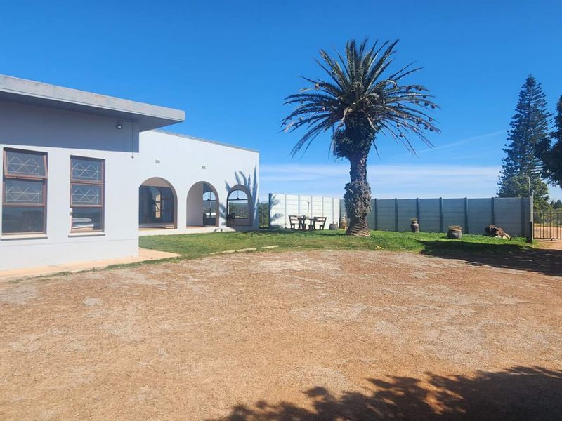 Rear exterior view of the farm property featuring an arched veranda, gravel driveway, and secure boundary walling.