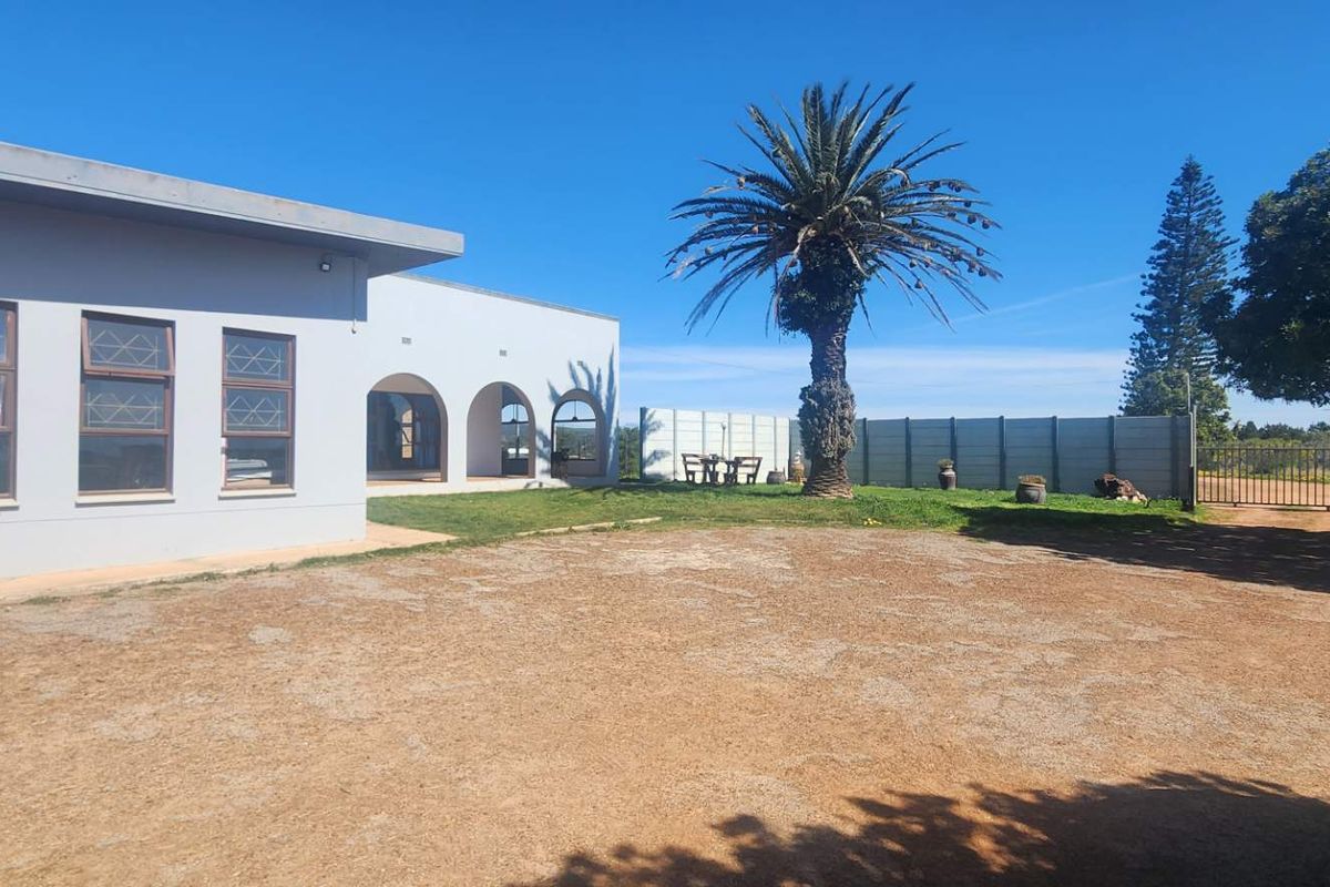 Rear exterior view of the farm property featuring an arched veranda, gravel driveway, and secure boundary walling.