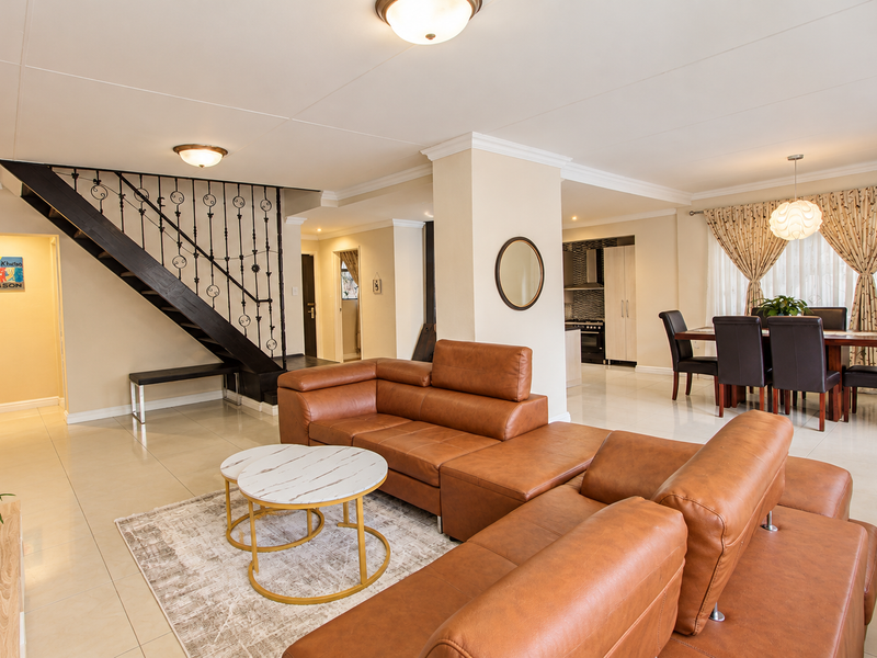 Spacious open-plan living and dining area featuring tiled floors, crown molding, and a distinctive staircase with a wrought iron balustrade.