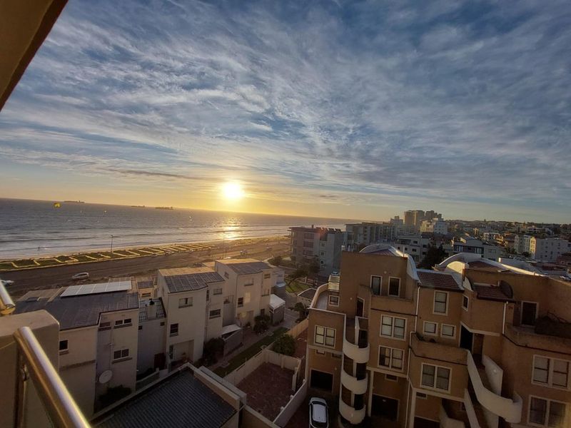 Elevated coastal view overlooking the ocean, beach, and surrounding residential apartment buildings at sunset.