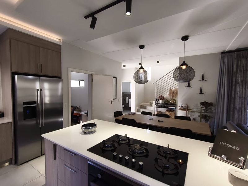Modern open-plan kitchen and dining area featuring a central island with gas hob, sleek cabinetry, and a staircase with contemporary balustrade.