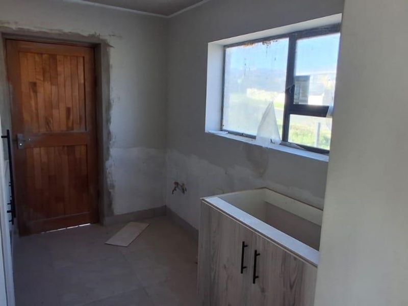 A partially finished scullery area featuring built-in cabinetry, a timber door, and tiled flooring, currently requiring final wall plastering and finishing touches.