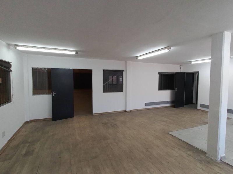Open plan industrial office space featuring neutral walls, fluorescent lighting, and a combination of wood-look and tiled flooring.