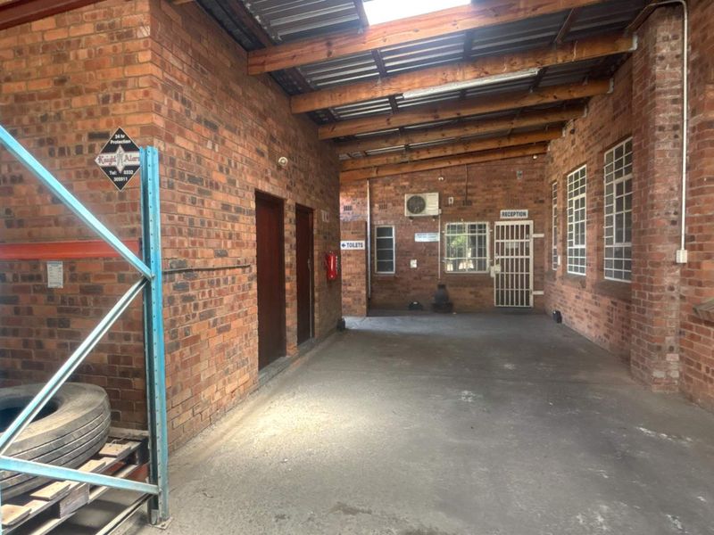 A functional industrial utility space featuring exposed brick walls, timber roof trusses, and concrete flooring, with secure access points and integrated air conditioning.