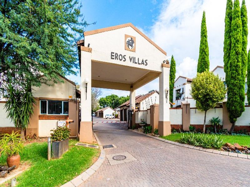 The main entrance gate and security access point for the Eros Villas apartment complex, featuring paved driveway and established landscaping.