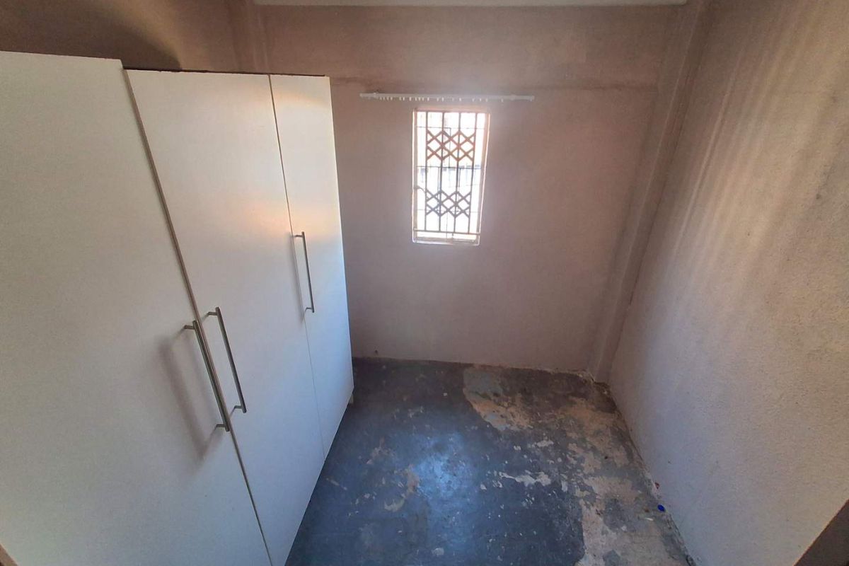 A small bedroom featuring a built-in wardrobe, a window with a security gate, and flooring in need of repair or replacement.