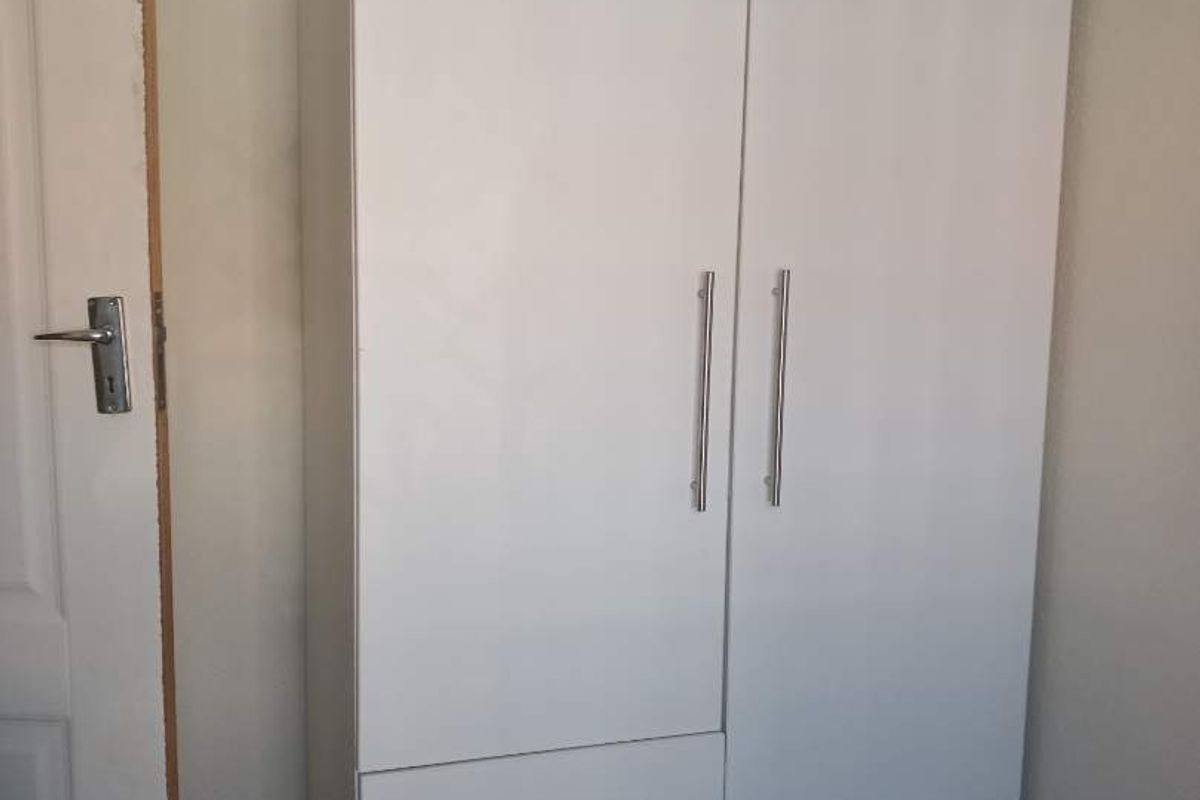 A bedroom featuring a white built-in wardrobe with integrated drawers and a standard interior door.
