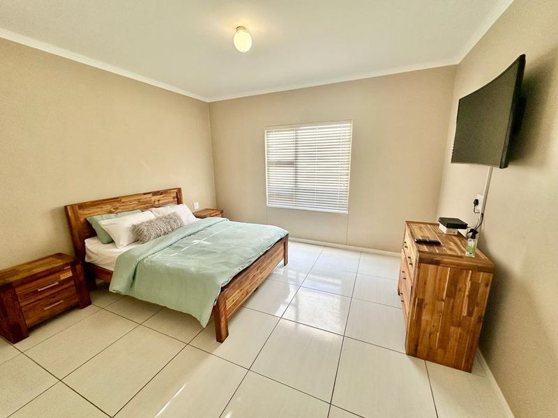A well-maintained bedroom featuring neutral wall tones, large format floor tiles, and a window fitted with venetian blinds.