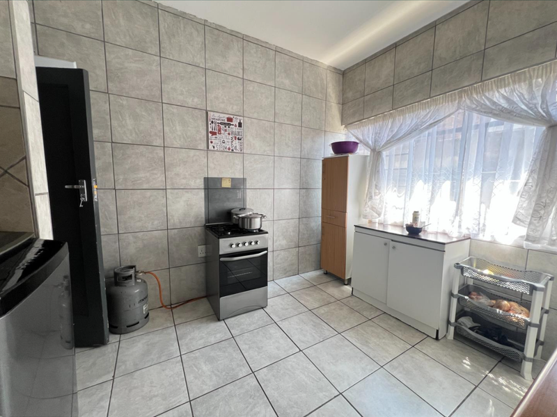 A functional kitchen featuring full-height wall tiling, tiled flooring, and a freestanding gas stove with built-in cabinetry.