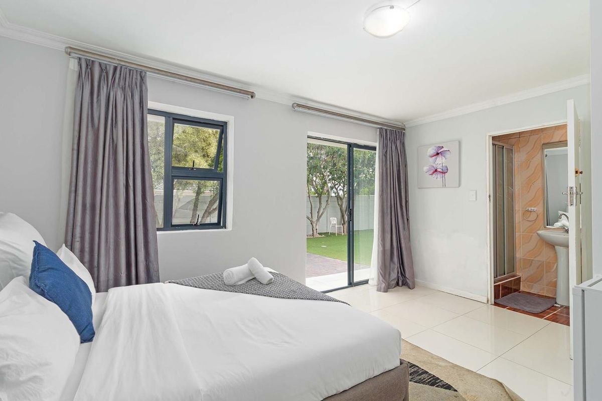 A bright bedroom featuring tiled flooring, direct access to the garden via a sliding glass door, and an attached en-suite bathroom with a shower.