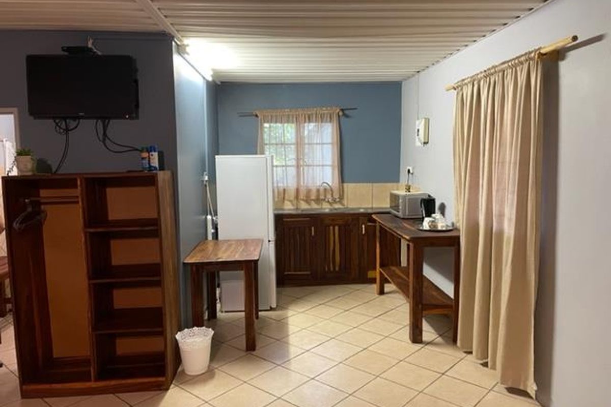 A functional kitchenette area featuring wooden cabinetry, tiled flooring, and a sink, integrated into a multi-purpose living space.