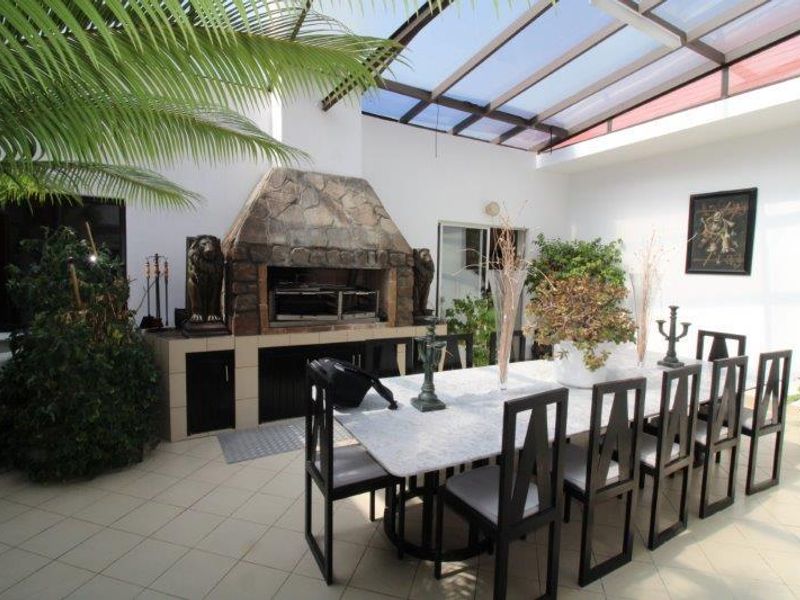 Covered patio area featuring a built-in stone braai, tiled flooring, and a translucent roof, ideal for outdoor dining and entertainment.