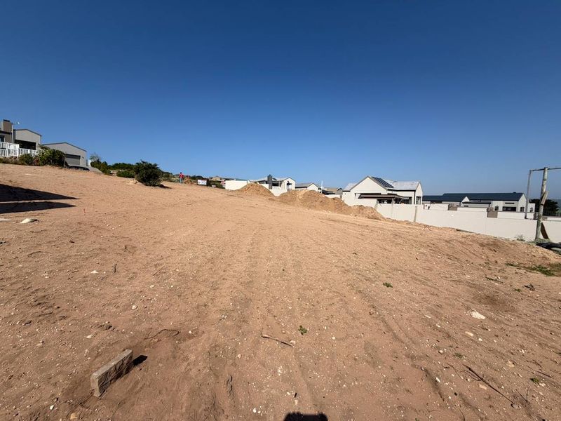 A vacant residential plot featuring a sloped landscape with surrounding boundary walls in an established neighborhood.