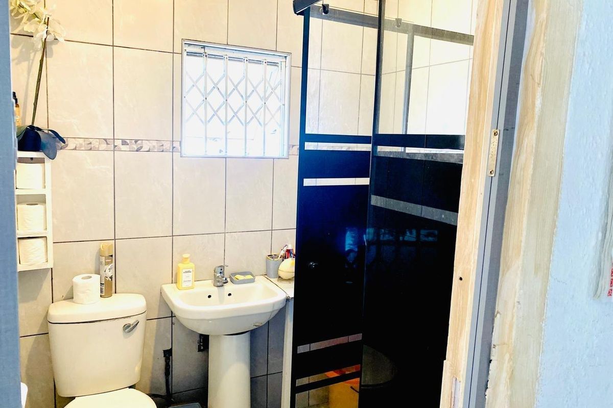 A functional bathroom featuring a pedestal basin, toilet, and a glass shower enclosure with tiled wall finishes.