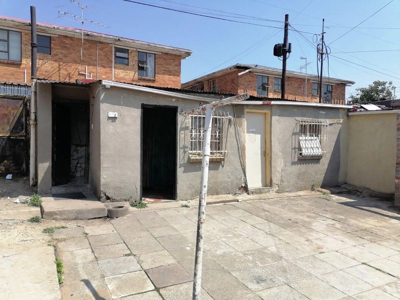 Rear exterior view of a residential property featuring a paved courtyard area with security bars on windows and weathered exterior wall finishes.