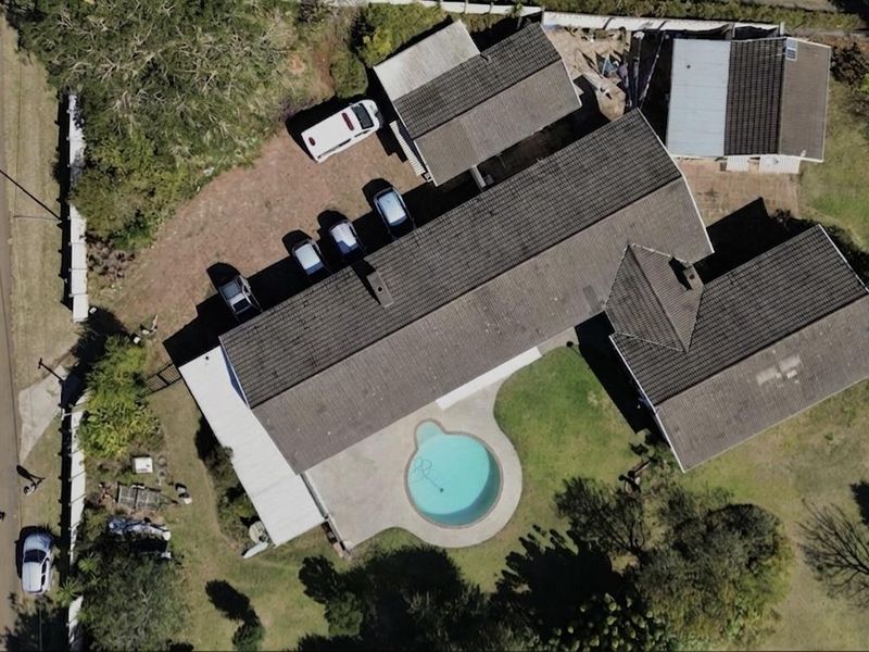 Aerial view of the property featuring a tiled roof house, a swimming pool, a driveway, and an outbuilding on a spacious lot.