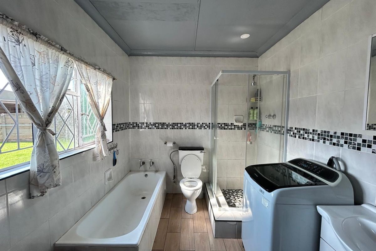 A functional bathroom featuring a built-in bathtub, separate glass-enclosed shower, toilet, and vanity, with tiled walls and wood-look flooring.