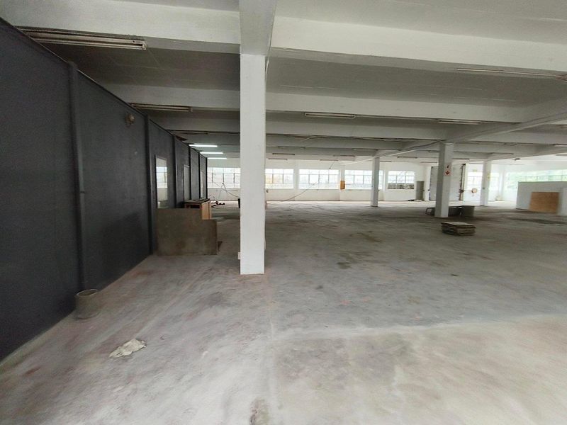 Spacious industrial warehouse area featuring concrete flooring, structural columns, and ample natural light through large windows, suitable for various commercial or storage uses.