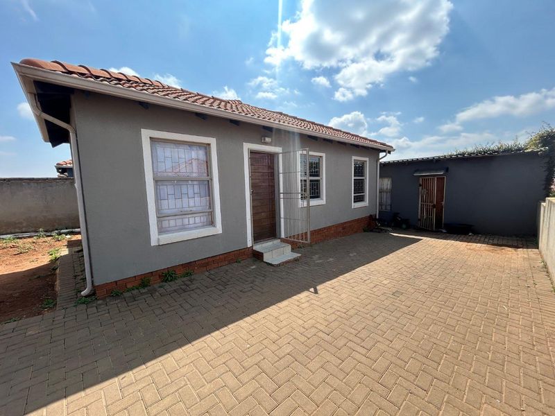 Rear view of the property featuring a paved courtyard, tiled roof, and secure access points with security gates.